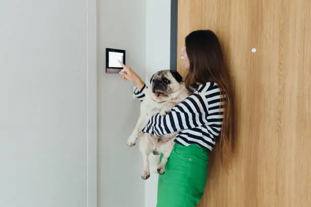 Smart home security for pet owners: A woman with her dog using a smart home device in her modern apartment, showcasing advanced pet-friendly technology.